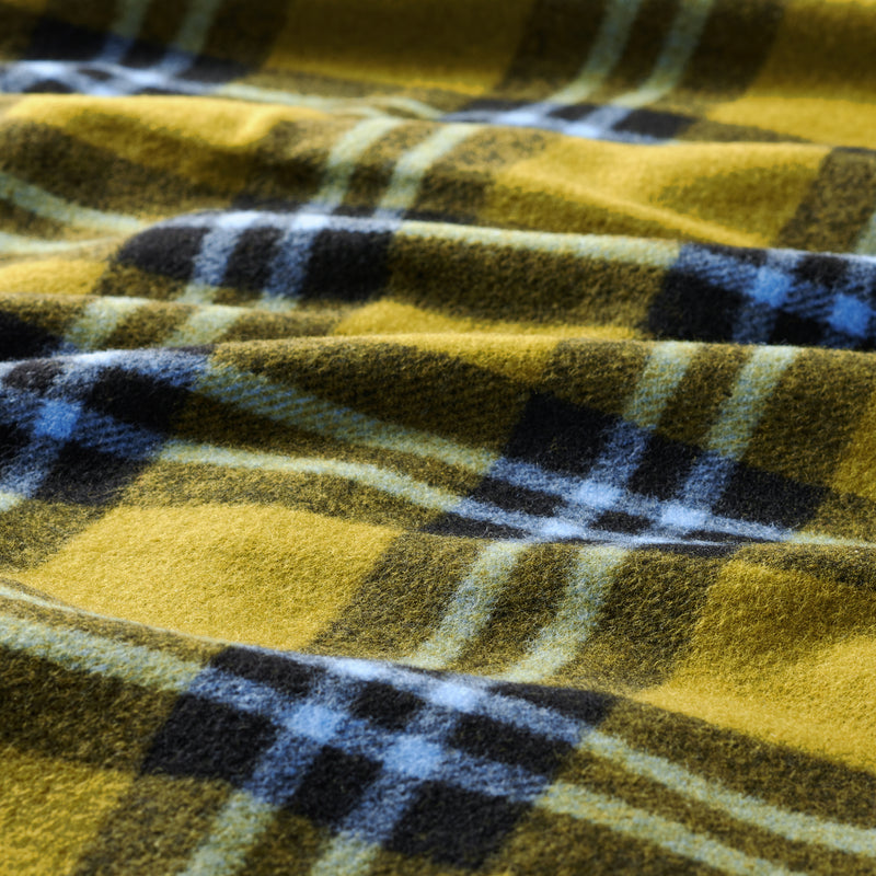 A closeup of a wool blanket, showing the wool surface texture and a green, black and blue plaid pattern.