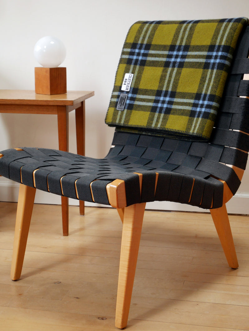 A green wool blanket with black and blue plaid. Its folded over a chair. 